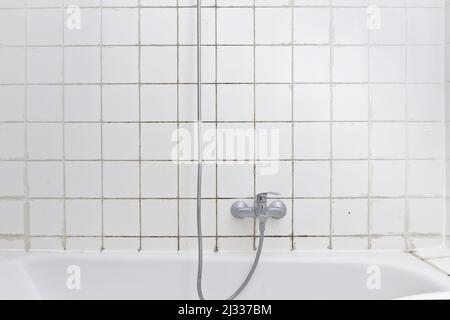 Location dommage concept: Douche sale dans la baignoire avec moisissure noire qui croît sur les calcifications sur le carrelage de ciment dans une vieille salle de bains négligée. Banque D'Images