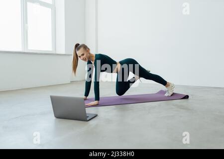 Active FIT sportif jeune femme exercice dans le salon à la maison sur tapis regarder en ligne vidéo entraînement tutoriel sport en direct cours d'entraînement sur ordinateur portable Banque D'Images