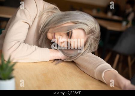 Portrait d'une jeune femme pensive attrayante avec de longs cheveux gris et un maquillage en sweat-shirt qui pose la tête à la main sur une table. Banque D'Images