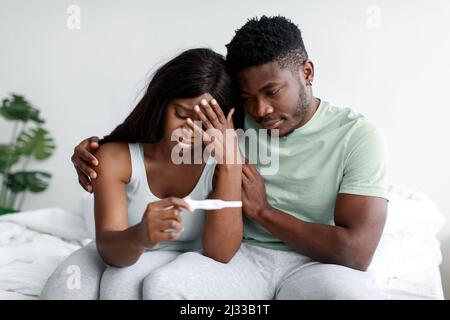 Les jeunes femmes et les hommes noirs en dépression triste bouleversement du test de grossesse négatif résultent dans l'intérieur de la chambre à coucher claire Banque D'Images