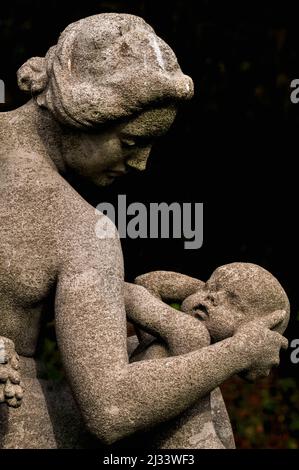 Une femme berce doucement la tête de son bébé alors qu'elle s'apprête à l'allaiter, dans ce détail d'« abondance » du sculpteur britannique Francis Derwent Wood (1871-1926). La statue, avec deux autres, forme la pièce maîtresse sculpturale de la roseraie de Hampton court, le palais royal historique fondé au 16e siècle à côté de la Tamise dans le quartier londonien de Richmond-upon-Thames, en Angleterre. Banque D'Images