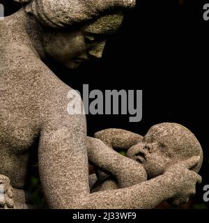 Une mère berce doucement la tête de son bébé alors qu'elle s'apprête à l'allaiter, dans ce détail carré d'abondance du sculpteur britannique Francis Derwent Wood (1871-1926). La statue, avec deux autres, forme la pièce maîtresse sculpturale de la roseraie de Hampton court, le palais royal historique fondé au 16e siècle à côté de la Tamise dans le quartier londonien de Richmond-upon-Thames, en Angleterre. Banque D'Images