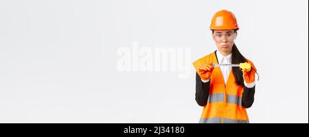 Déçue femme asiatique ingénieur de construction, architecte montrant petite taille sur mètre ruban, en poudant contrarié avec des mesures, debout Banque D'Images