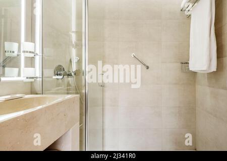 salle de bains avec lavabo en marbre couleur crème, miroir sans cadre avec éclairage intégré et cabine de douche Banque D'Images