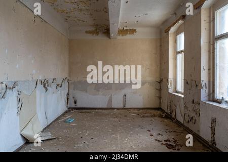 Vider la vieille chambre dans un bâtiment abandonné. La lumière de la fenêtre brille. La peinture s'écaille des murs avant la rénovation. Intérieur du chantier de construction. Banque D'Images