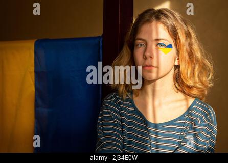 Fille ukrainienne - une adolescente avec un coeur peint jaune-bleu près de son œil, mise en évidence par une bande de lumière du soleil. Concept d'espoir et de foi parmi la civ Banque D'Images