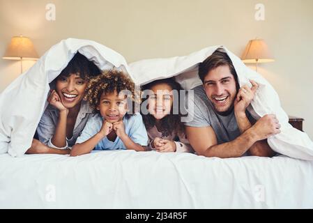 La maison est l'endroit le plus cozien. Portrait d'une famille heureuse se reposant ensemble sous une couverture à la maison. Banque D'Images