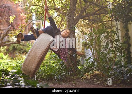 Des journées d'été insouciantes d'une enfance idyllique. Un préadolescent balançant sur une balançoire de pneu dans le jardin. Banque D'Images