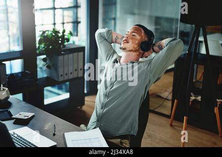 Écouter mon podcast favori. Photo d'un jeune homme d'affaires portant un casque tout en prenant une sieste dans un bureau. Banque D'Images