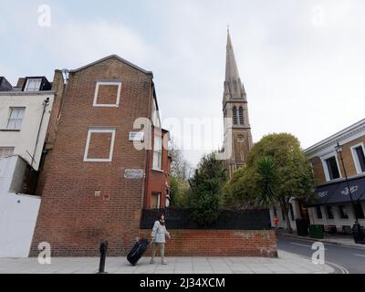 Une femme avec une valise à roulettes marche le long de la route de Moscou à Bayswater avec l'église St Matthews Bayswater derrière. Londres Banque D'Images