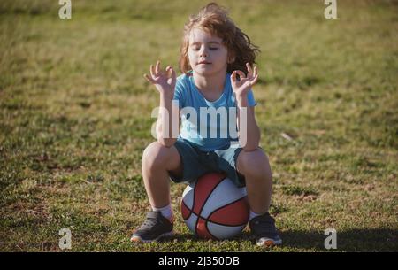 Un écolier assis sur le terrain de basket-ball et se détendre. Jeune sportif fatigué assis avec un ballon de basket à l'aire de jeux. Banque D'Images