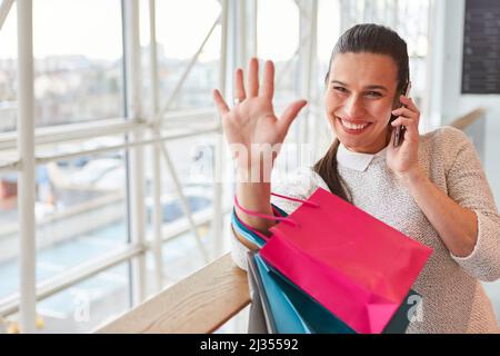 Jeune femme avec beaucoup de sacs de shopping agitant et parlant sur le téléphone portable après le shopping Banque D'Images