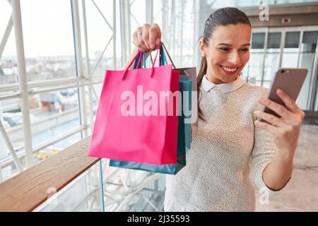 Jeune femme souriante utilisant un smartphone chat vidéo après avoir fait du shopping en tenant des sacs Banque D'Images