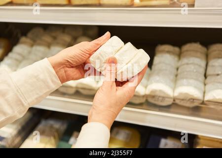 Le client à la tablette réfrigérée tient le fromage doux dans ses mains pendant qu'il magasinait au supermarché Banque D'Images