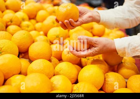 Les mains d'un client tiennent des oranges lorsqu'il fait ses achats sur le marché ou dans un supermarché Banque D'Images