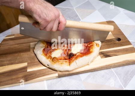Un homme qui coupe une pizza maison sur une planche à découper en bois à l'aide d'une grande trancheuse à pizza. Autriche Banque D'Images