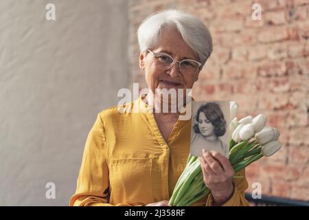 Jour de grand-mère photo moyenne d'une grand-mère portant une chemise jaune ensoleillée tenant des fleurs et photo noir et blanc de sa version plus jeune. Photo de haute qualité Banque D'Images