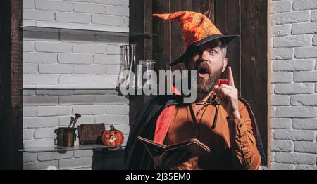 Homme face effrayant avec l'horreur maquillage tenant la tête de citrouille lanterne jack sur fond de ciel. Sorcellerie mal avec cheveux rouges et barbe dans un manteau noir de lecture Banque D'Images