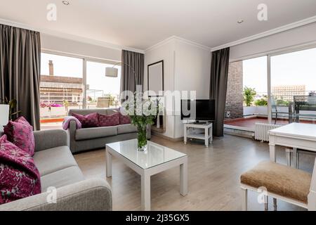 Séjour d'un appartement de grand standing avec deux grandes terrasses, canapés en tissu gris, mobilier en bois blanc et coussins violets Banque D'Images