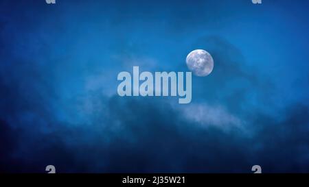 Une belle vue de la pleine lune lumineuse qui se hante à travers les nuages sombres dans le ciel nocturne Banque D'Images