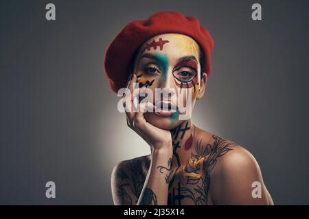 La créativité prend du courage. Photo studio d'une jeune femme posant avec de la peinture sur son visage sur un fond gris. Banque D'Images
