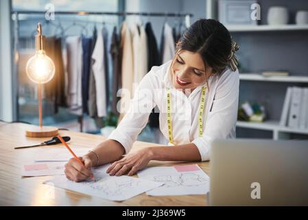 Travailler sur de nouvelles conceptions. Photo courte d'une jeune créatrice de mode qui travaille sur ses créations dans son atelier. Banque D'Images