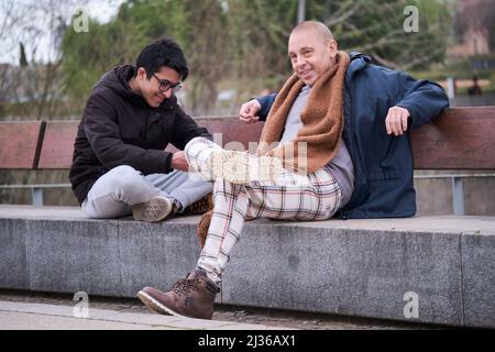 Père et fils adolescent parlant et riant assis sur un banc dans un parc. Banque D'Images