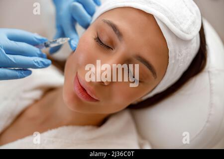 Belle jeune femme recevant l'injection d'acide hyaluronique dans les pommettes au salon de beauté Banque D'Images