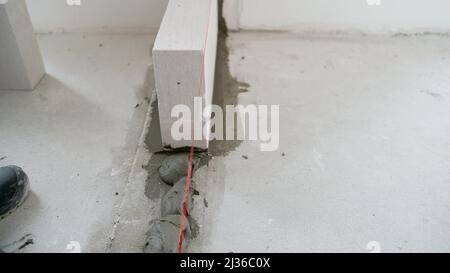 Un travailleur érige un mur de blocs de béton cellulaire dans un appartement. Installation de la première rangée de blocs de béton cellulaire. Le travailleur commence le sapin Banque D'Images