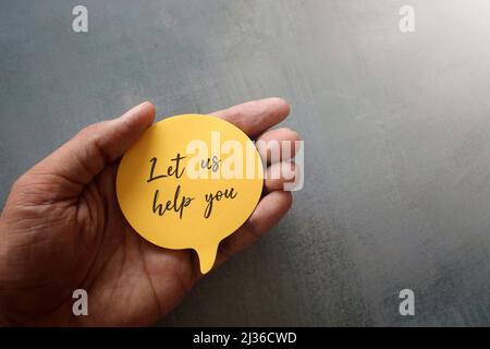 Main tenant la bulle de la parole avec le texte "Laissez-nous vous aider" avec l'espace de copie pour le texte. Banque D'Images