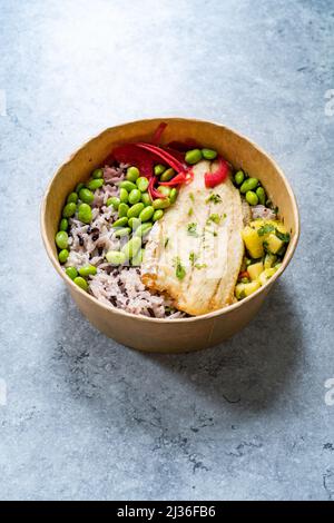 Bol à poisson avec filet de poisson et haricots d'Edamame, riz basmati, pickle d'oignon et cube de ananas haché dans un conteneur à emporter en plastique Banque D'Images