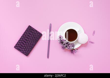 Une tasse de thé, des carnets, un stylo, un bouquet de lilas sur fond violet. Fleurs de printemps pourpres. Pause thé au travail blogueur ou employé de bureau Banque D'Images