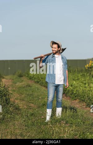 vue sur toute la longueur de jeune fermier avec pelle souriante dans le champ Banque D'Images