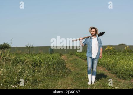 vue sur toute la longueur de happy farmer marchant avec une pelle sur le terrain vert Banque D'Images