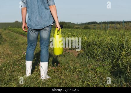 vue partielle du fermier dans des bottes en caoutchouc blanc debout avec arrosoir jaune dans le champ Banque D'Images