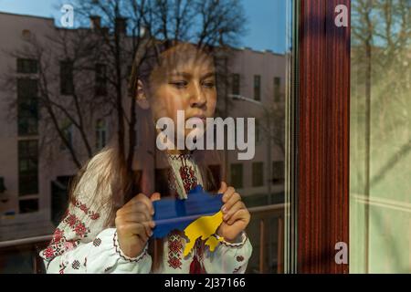 Une fille dans une robe brodée regarde par la fenêtre, tient une carte de l'Ukraine peinte en bleu et jaune dans ses mains.la fille proteste contre la guerre Banque D'Images