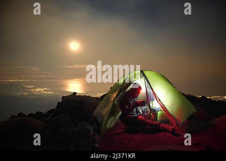 PARC ETNA, SICILE, ITALIE - 22 DÉCEMBRE 2018 : un homme est assis et buvant dans une tente illuminée à haute altitude dans le parc Etna avec vue sur le sicil Banque D'Images