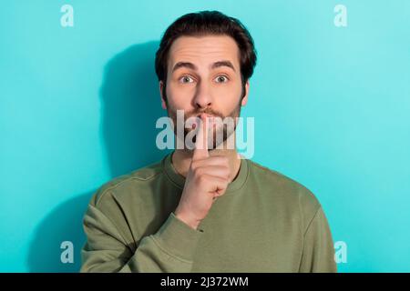 Photo de la barbe silencieuse jeune gars doigt bouche porter un sweat-shirt kaki isolé sur fond de couleur sarcelle Banque D'Images