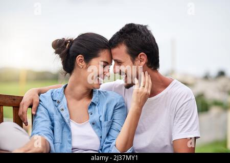 Il n'y a pas de meilleur sentiment que l'amour. Photo courte d'un jeune couple affectueux assis sur un banc à l'extérieur. Banque D'Images