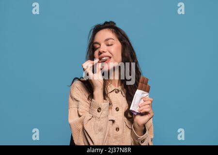 Joyeuse femme européenne millénaire heureuse avec les yeux fermés aime le goût de la barre de chocolat Banque D'Images