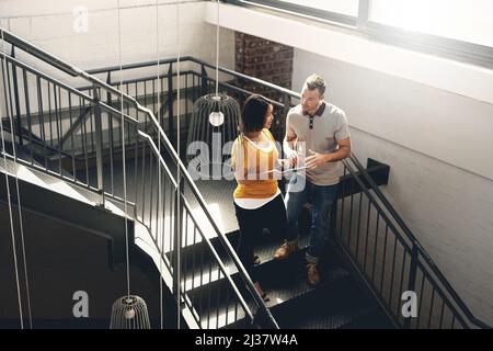 Gérer quelques idées après un collègue. Photo en grand angle de deux jeunes designers regardant une tablette numérique tout en marchant dans un escalier. Banque D'Images
