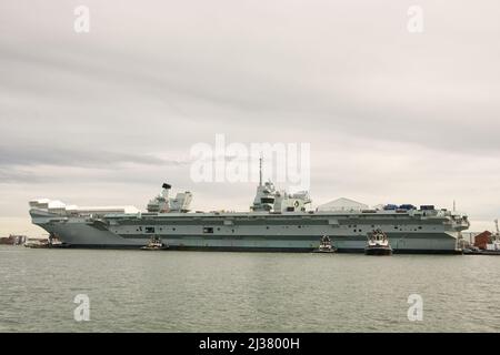 Le porte-avions Queen Elizabeth amarré au chantier naval de Portsmouth, dans le Hampshire, en Angleterre. Avec tugs présents. Vue depuis le bateau sur l'eau. Banque D'Images
