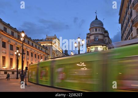 Tram passant par la rue Avenida de la Constitución au crépuscule avec le bâtiment la Adriatica à Séville Andalousie Espagne. Banque D'Images