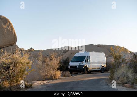 Une fourgonnette Dodge blanche est garée dans un camping entouré d'énormes rochers dans le terrain de camping Jumbo Rocks, dans le parc national Joshua Tree, dans le sud de la Californie. Banque D'Images