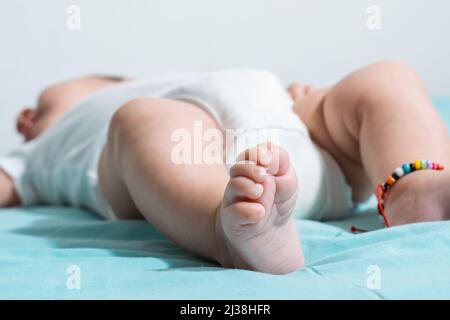 belle et tendre pieds d'une petite fille de deux mois, avec ses petits orteils bien rétractés, elle est habillée dans une barboteuse blanche. allongé sur un lit Banque D'Images