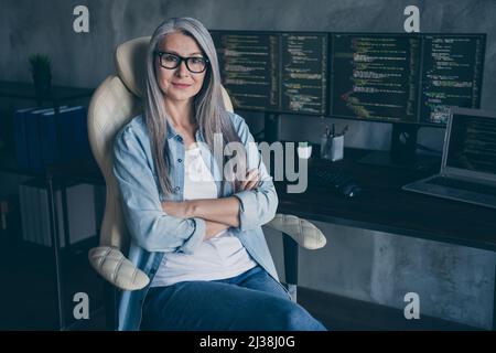 Portrait d'une femme âgée réussie chaise assise bras croisés regarder caméra web design lieu de travail à l'intérieur Banque D'Images