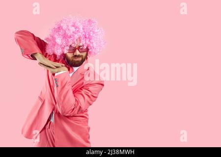Homme drôle en costume de fête rose, perruque clown et verres funky dansant sur fond rose copie espace Banque D'Images