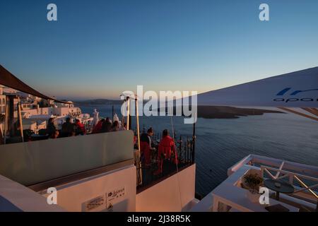 Santorini, Grèce - 10 mai 2021 touristes assis sur une terrasse d'un bar en plein air et profitant de la vue panoramique sur le magnifique coucher de soleil de Santorini Banque D'Images