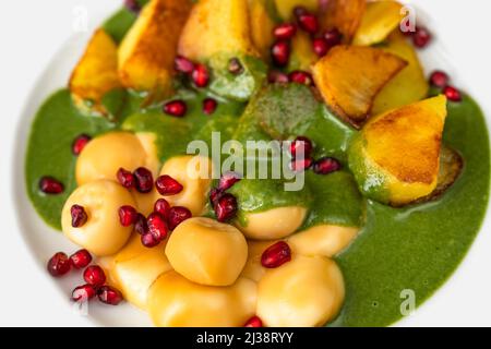 Boulettes de fromage fumé, pommes de terre frites, sauce aux épinards et graines de grenade sur une assiette blanche, dîner végétarien, gros plan. Banque D'Images