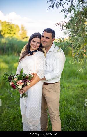 Mariée et marié le jour du mariage en marchant à l'extérieur sur la nature printanière. Couple de mariée, femme et homme heureux et récemment mariés s'embrassant dans le parc vert. Couple de mariage amoureux à l'extérieur. Mariée et marié. Banque D'Images